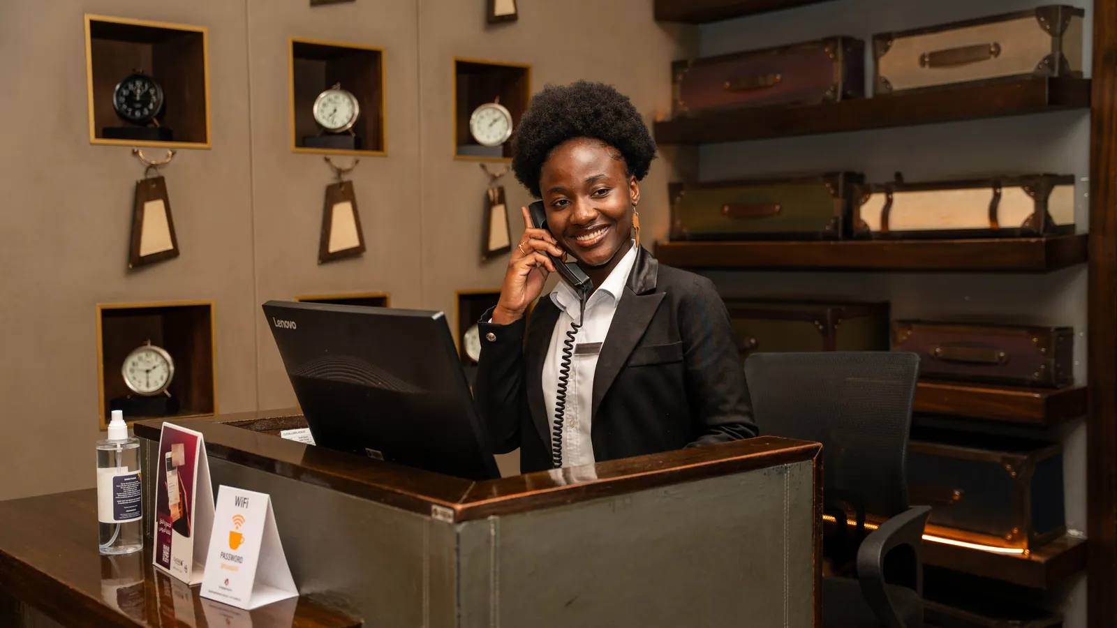 Au comptoir de réception d’un hôtel, une jeune femme en tenue prend un appel avec le sourire.