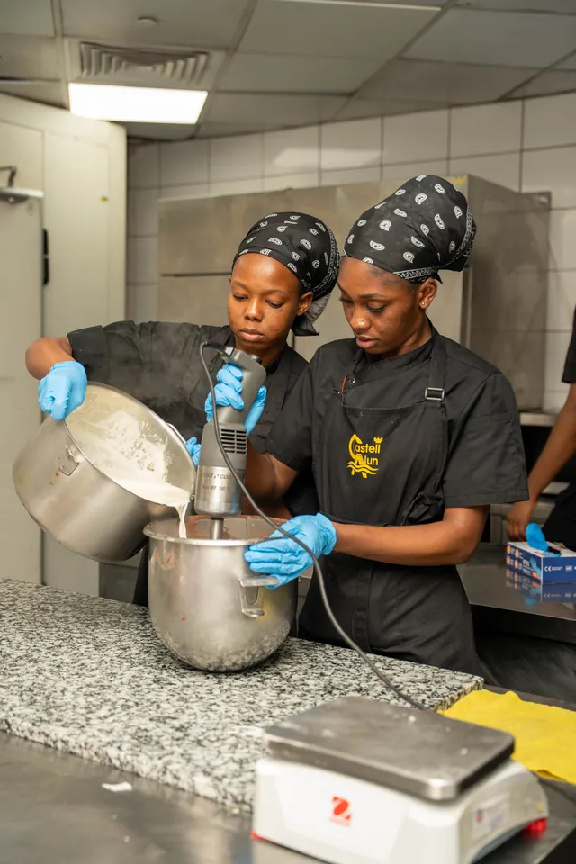 Deux étudiantes versent une préparation dans la cuve du batteur, au laboratoire.