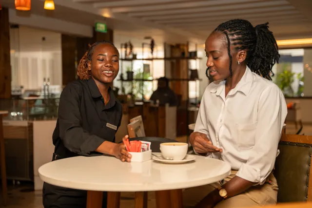 À la table d’une cliente, une étudiante prend le temps de l’échange, café servi.