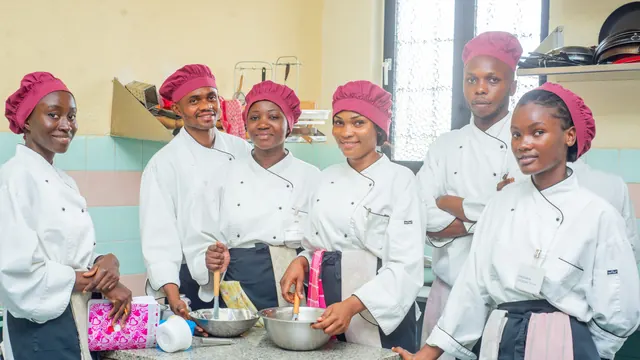Six étudiants en veste blanche et toque bordeaux, réunis autour du plan de travail de la cuisine pédagogique.