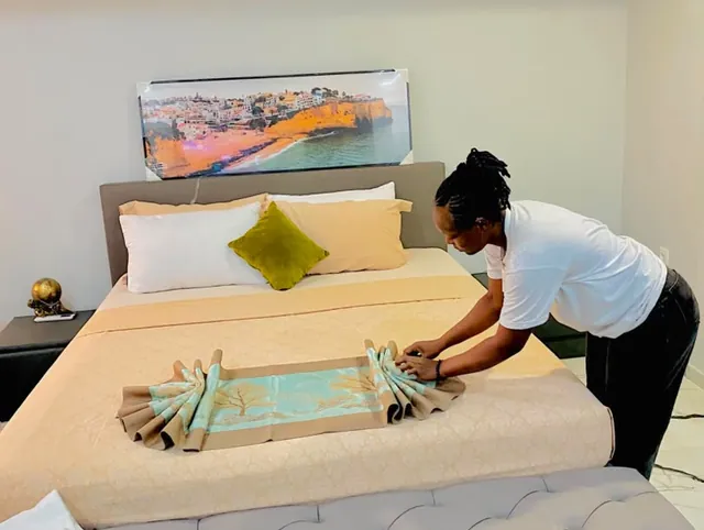 Une étudiante en tenue d’étage fait le lit d’une chambre d’hôtel, serviette pliée en décoration.