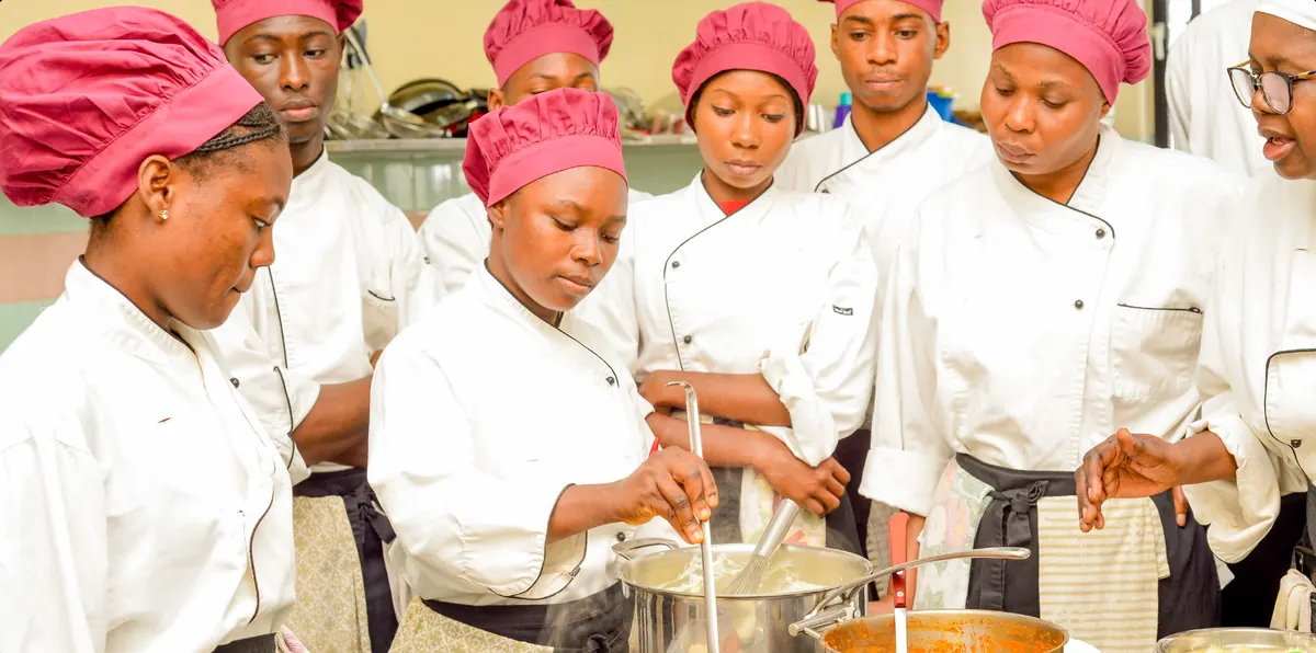 Un groupe d’étudiants en toque entoure une formatrice lors d’une démonstration culinaire.