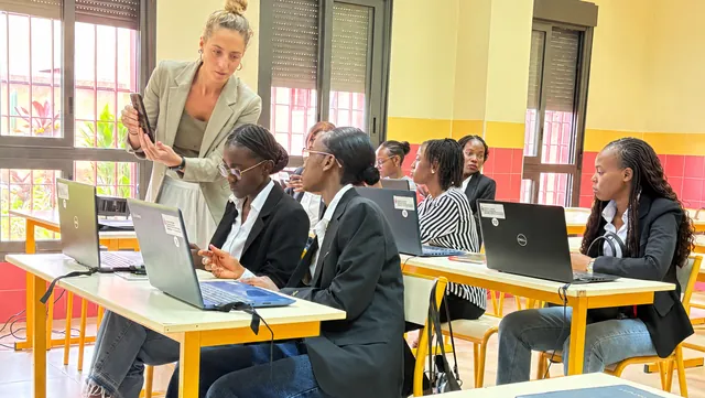 Des étudiantes en salle de cours devant leurs ordinateurs portables, accompagnées par une formatrice.