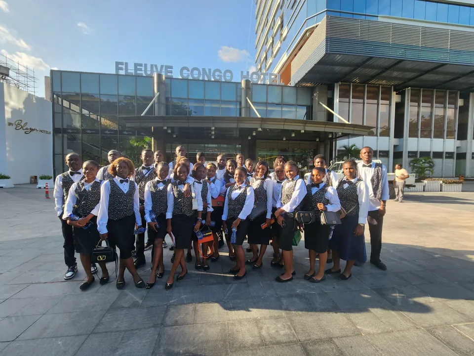 La promotion en tenue de service, réunie devant l’entrée du Fleuve Congo Hotel à Kinshasa, enseigne de l’hôtel au-dessus d’elle.